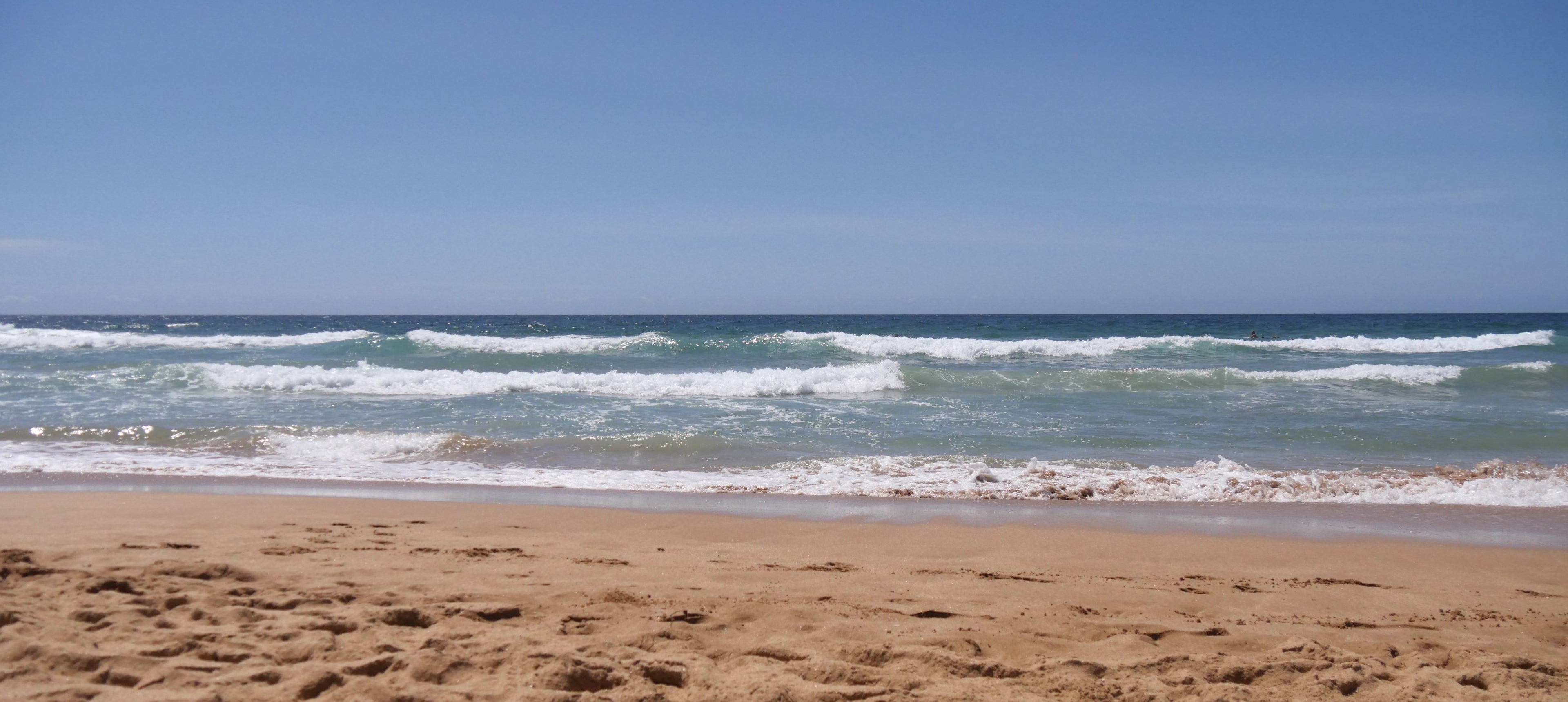 A photograph of the sunny beach with waves, looking over the ocean's horizon.